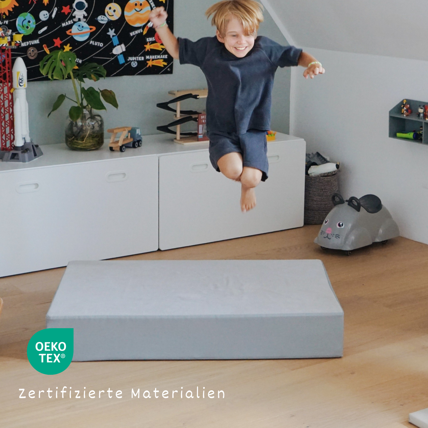 Kleinkind springt auf malwim Hüpfpolster Webstoff Stahlgrau/Grau – Bewegungsfreude zu Hause
